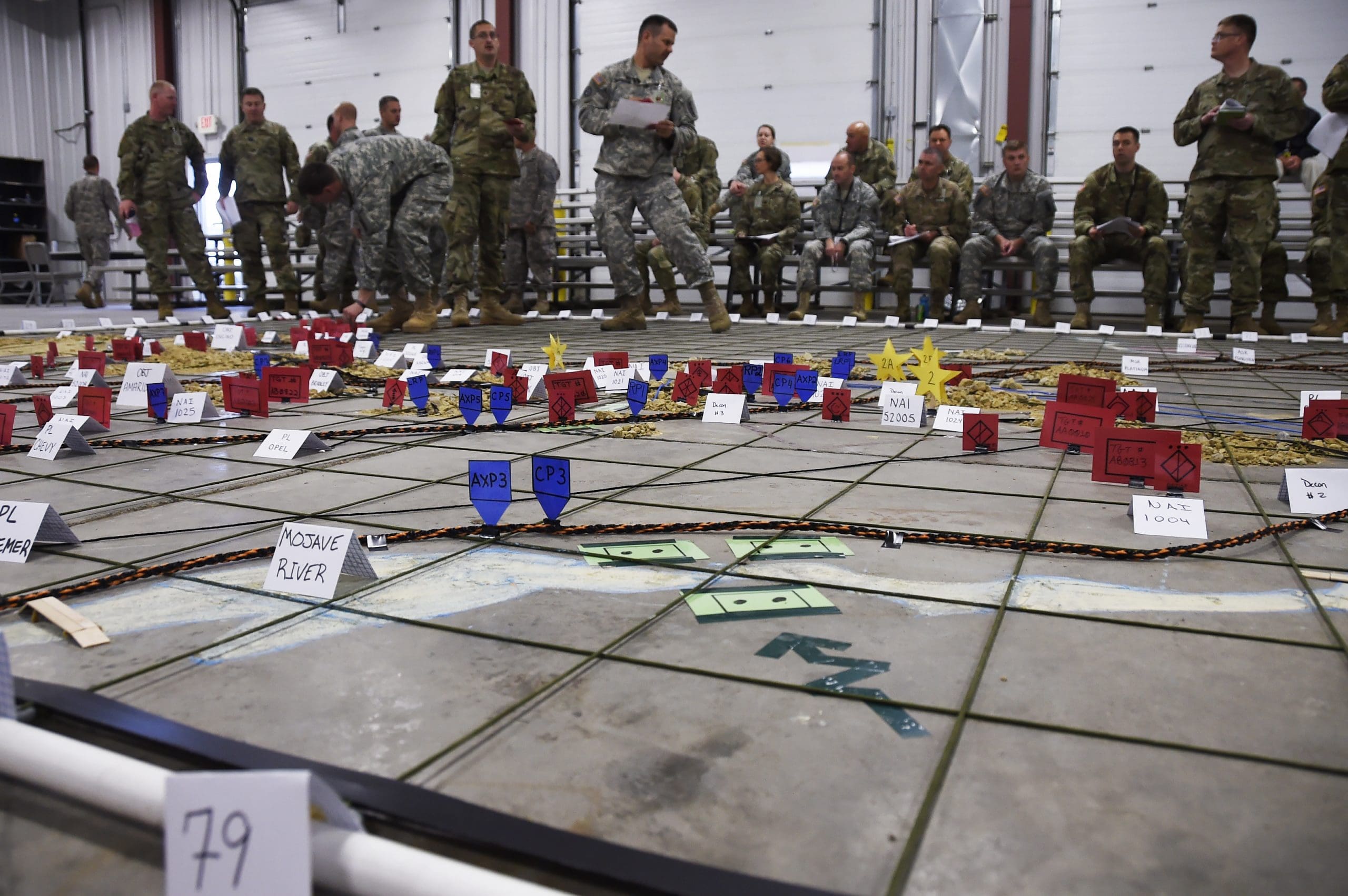 Staff officers and battalion leadership position visual aids — representing brigade assets, phase lines, objectives and enemy units — on a large situation map in a maintenance bay at Fort McCoy, Wis., Aug. 26 as part of a Warfighter combined arms rehearsal. The rehearsal was a walk-through allowing the brigade’s subordinate battalions to indicate their position and actions at various stages of the mock campaign. Wisconsin Department of Military Affairs photo by Vaughn R. Larson