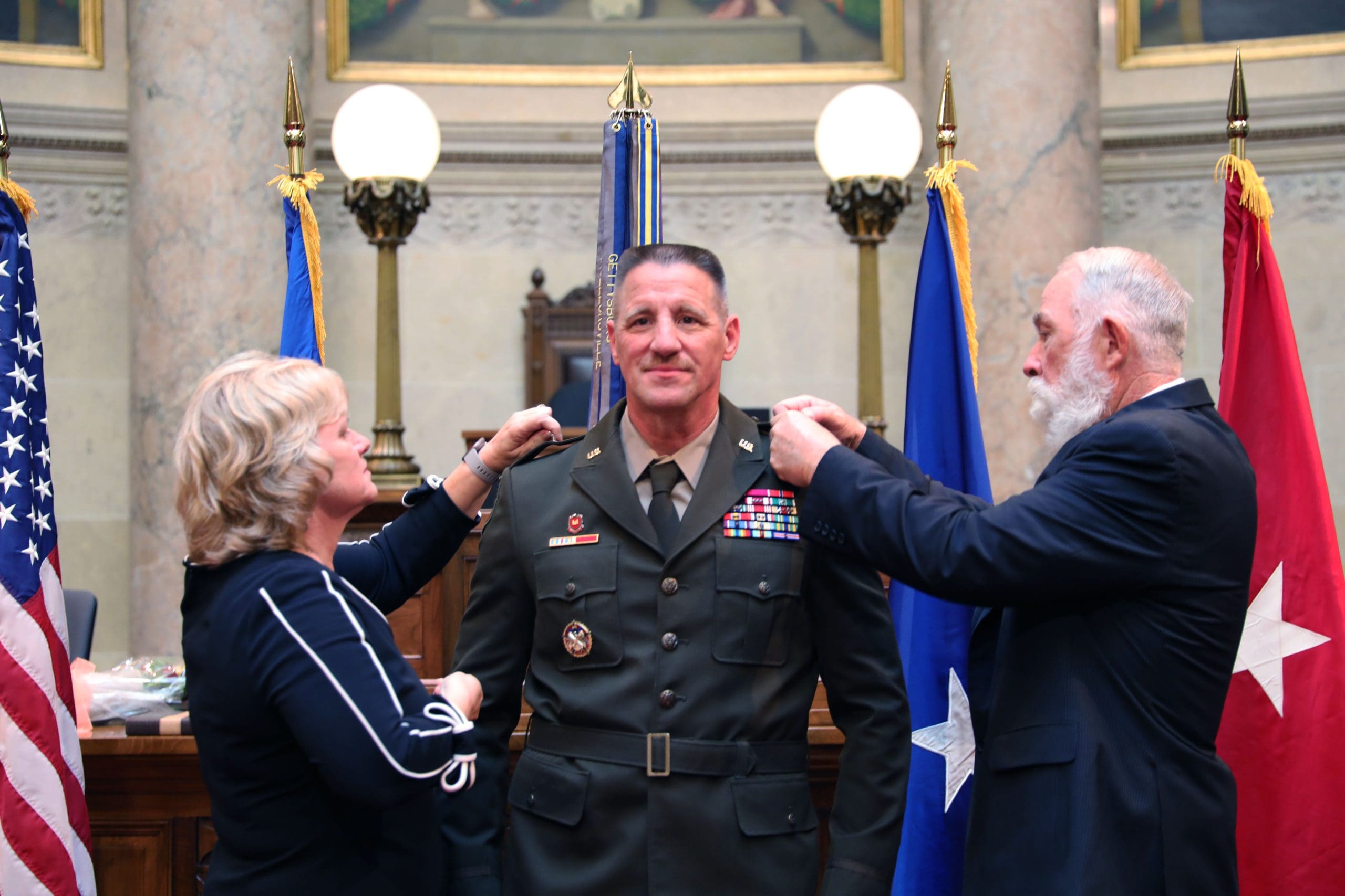 Col. Pulvermacher is pinned with his new rank of Brig. Gen. by his wife, Doris, and his first active duty squad leader, Sgt. 1st Class Retired Robert “Sam” Nation during a Sept. 24 ceremony at the Wisconsin State Capitol in Madison, Wis. Pulvermacher was promoted to brigadier general and will assume the role of Deputy Director of Acquisitions for the National Guard Bureau.