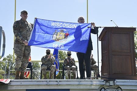 Gov. Tony Evers presents Capt. Shawn Smith, commander of the Wisconsin Army National Guard’s 107th Maintenance Company, with a state flag during a formal sendoff ceremony at Sparta Memorial Field in Sparta, Wis., May 29. The 107th is based in Sparta, with detachments in Viroqua, Wis., and Camp Ripley, Minn. The unit is deploying to Eastern Europe to perform maintenance and recovery operations in support of Operation Atlantic Resolve and the Defender-Europe 2021 multinational joint exercise. Wisconsin Department of Military Affairs photo by Vaughn R. Larson